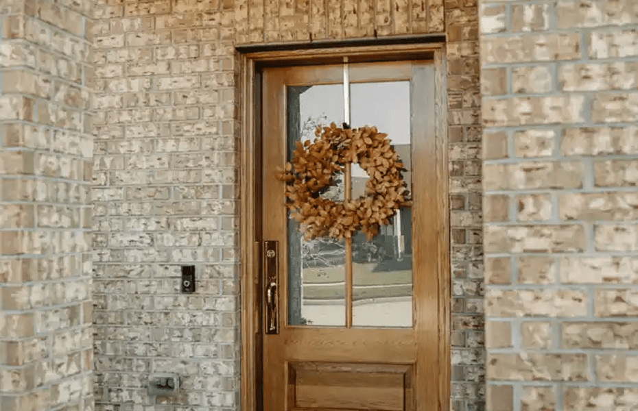 Wooden front door with glass panel and autumn wreath hanging on brick exterior wall